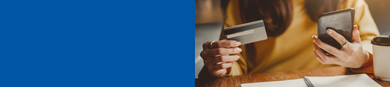 Woman in yellow holding a visa card and an iPhone at a desk.