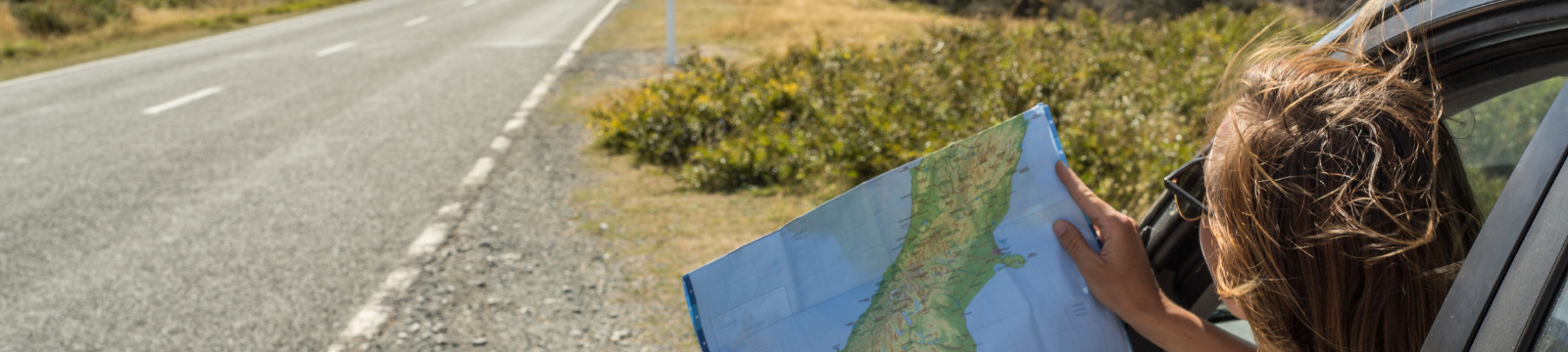 Woman hanging out a car window with a roadmap from the side of a road