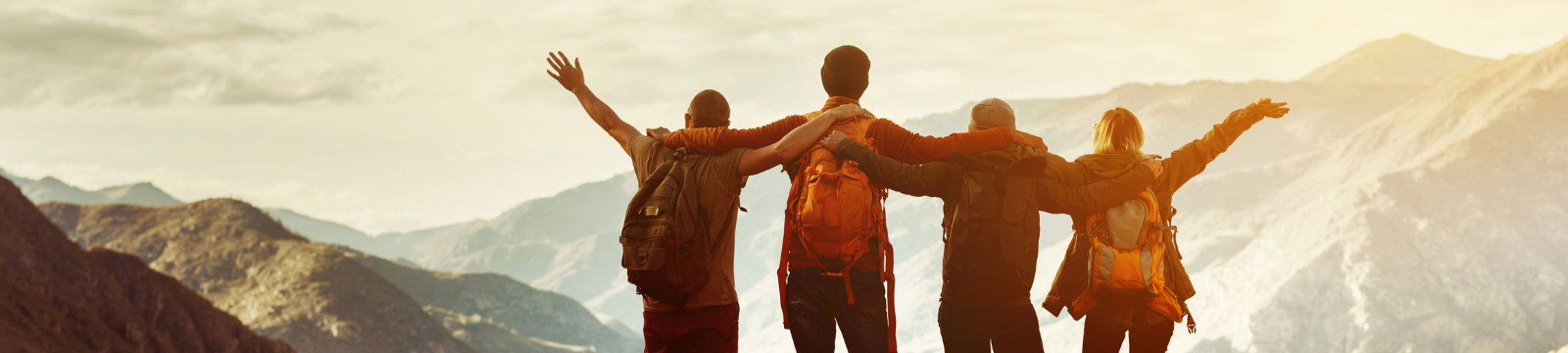 Four people on a mountain with hands in the air. 
