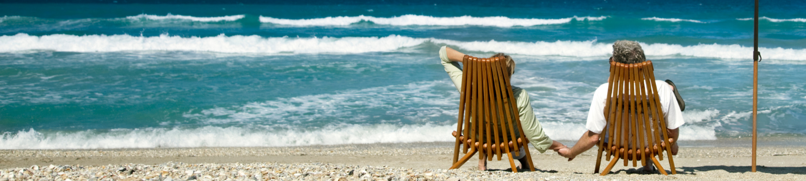 Man and woman sitting on the beach with an umbrella.