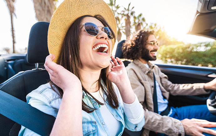 Couple driving with the top down in their new car.